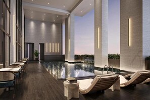 A modern indoor pool area with lounge chairs, a long table, and a waterfall feature. - Rhythm Gurugram - Hotel & Suites (GURUGRAM)