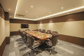 A conference room with a long table, multiple chairs, and a flat-screen TV mounted on the wall.