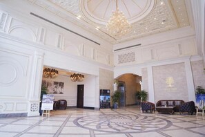 A spacious lobby with a grand chandelier, a reception desk, and seating area.