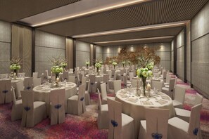 A spacious banquet hall with round tables, white chairs, and floral centerpieces. - Rhythm Gurugram - Hotel & Suites (GURUGRAM)