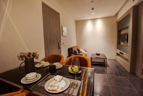 A modern living room with a dining area, a sofa, a TV mounted on the wall, and a small table with a vase of flowers.