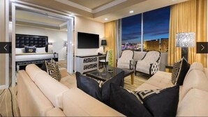 Un hotel moderno con una cama grande, un área de estar con sofás y sillones, un televisor de pantalla plana y vistas a la ciudad a través de la ventana.