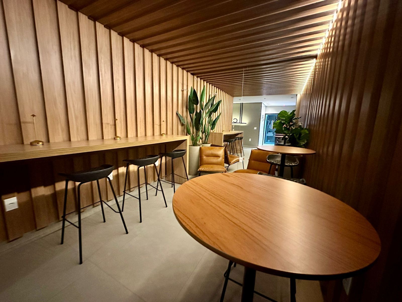 Un área de bar moderna con listones de madera en las paredes, una barra larga y varios taburetes.