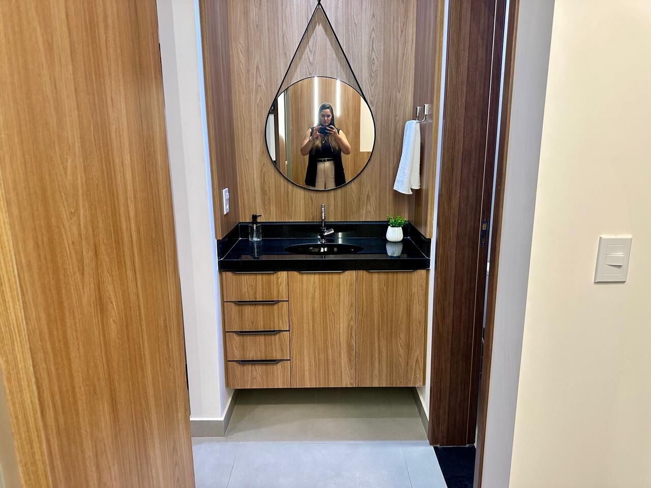 Een moderne badkamer met een houten wastafelmeubel, een zwart aanrecht en een ronde spiegel.