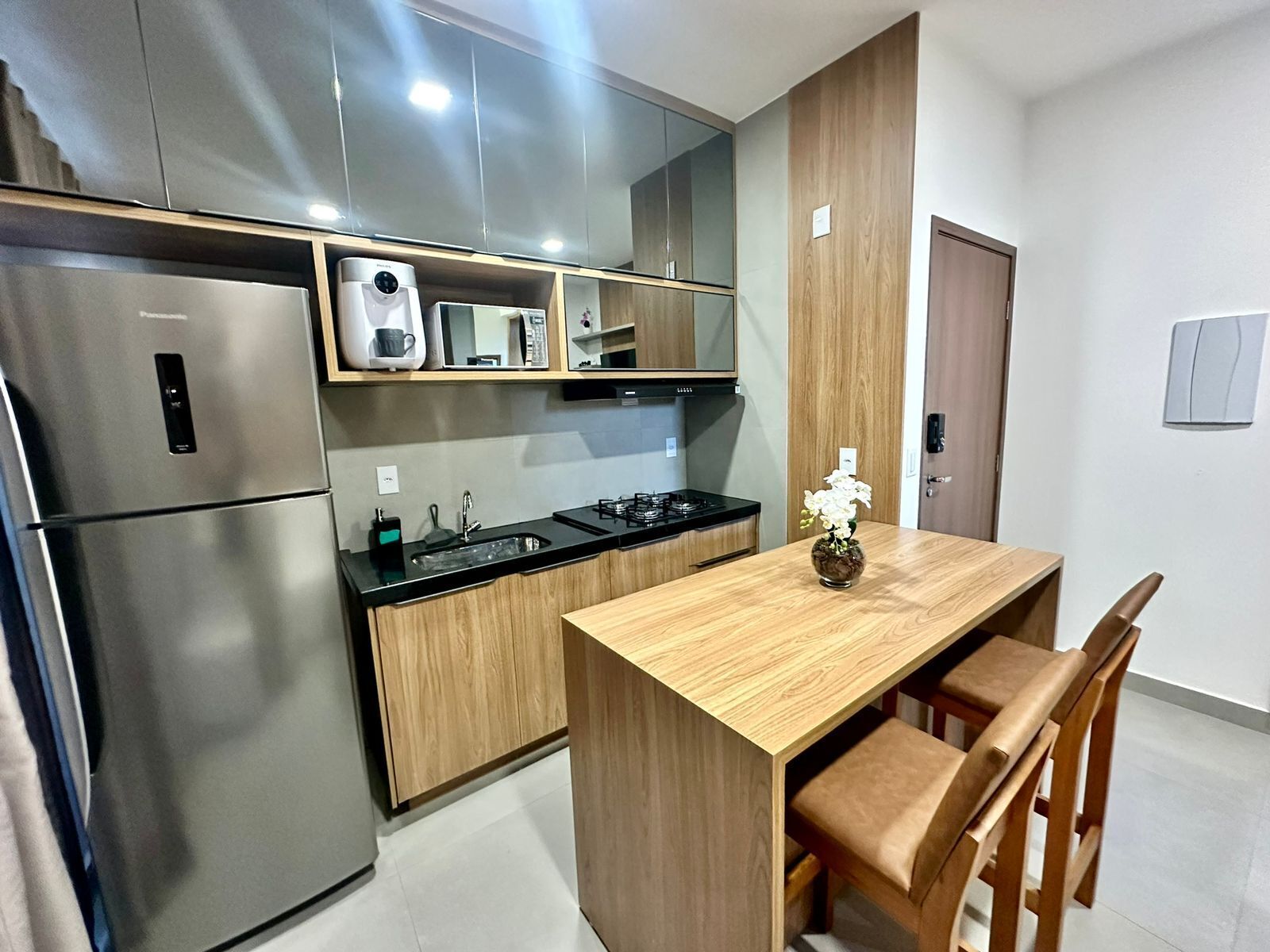 A modern kitchen with stainless steel appliances, wooden cabinets, a black countertop, and a wooden dining table with two chairs.
