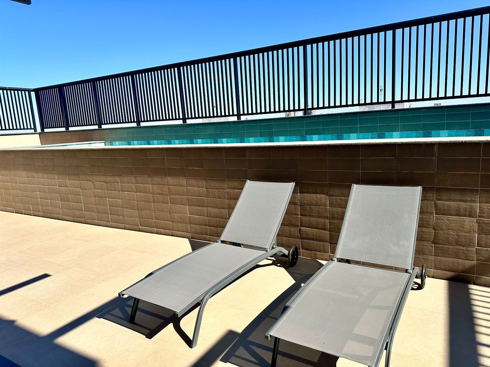 Un espace aménagé au bord de la piscine, avec deux chaises longues et une rambarde en métal.