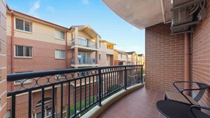 A balcony with a metal railing, a brick wall, and a view of neighboring buildings.