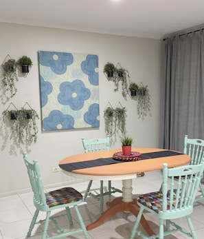 A dining area with a round table, four chairs, a wall-mounted painting, and hanging planters.