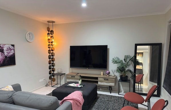 A modern living room with a flat-screen TV, a sofa, a coffee table, a decorative wall piece, and a potted plant.