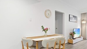 Een moderne eetruimte met een ronde tafel, vier stoelen, een klok, een deur, een televisie en een vaas met bloemen.