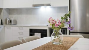 A modern kitchen with white cabinets, a stainless steel refrigerator, and a vase with flowers on a table. - KozyGuru | Camperdown | Stylish Apt with Parking (Camperdown)