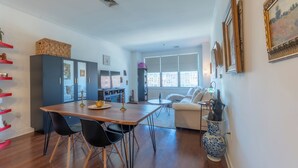 A modern living room with a dining area, a sofa, and a large window providing natural light.