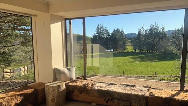 A modern room with a large window, a wooden bench with a fur throw, and a patterned rug.