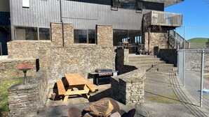 A modern building with stone walls, a patio with a barbecue grill, and a fire pit.