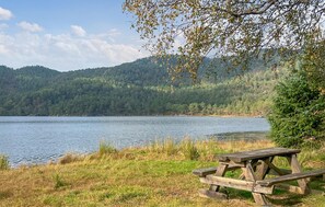 Een picknickplaats aan het meer, met een houten bank en uitzicht op een bebost berglandschap.