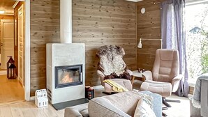 A cozy cabin interior with a fireplace, wooden walls, a comfortable seating area, and a large window with curtains.