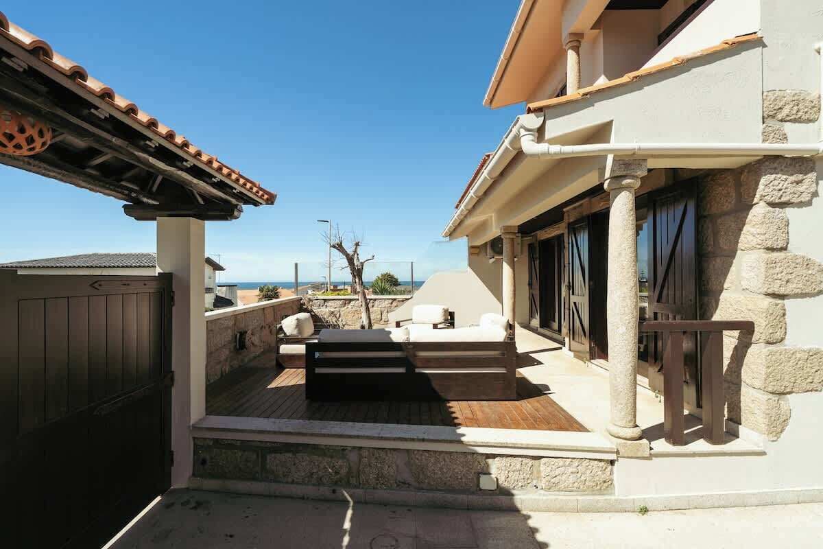 Une terrasse extérieure couverte, dotée d’un plancher en bois, de colonnes en pierre et offrant une vue sur la mer.