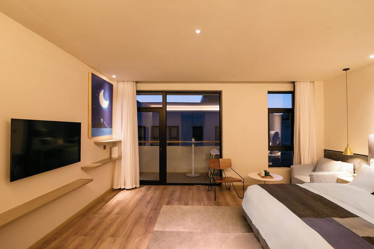 Een moderne hotelkamer met een flatscreen televisie, een groot raam met gordijnen, een bank, een klein rond tafeltje en een bed.