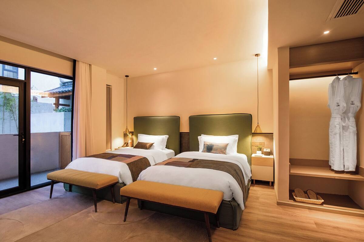 Een hotelkamer met twee bedden, een bankje, een kledingrek en uitzicht op het omliggende landschap.