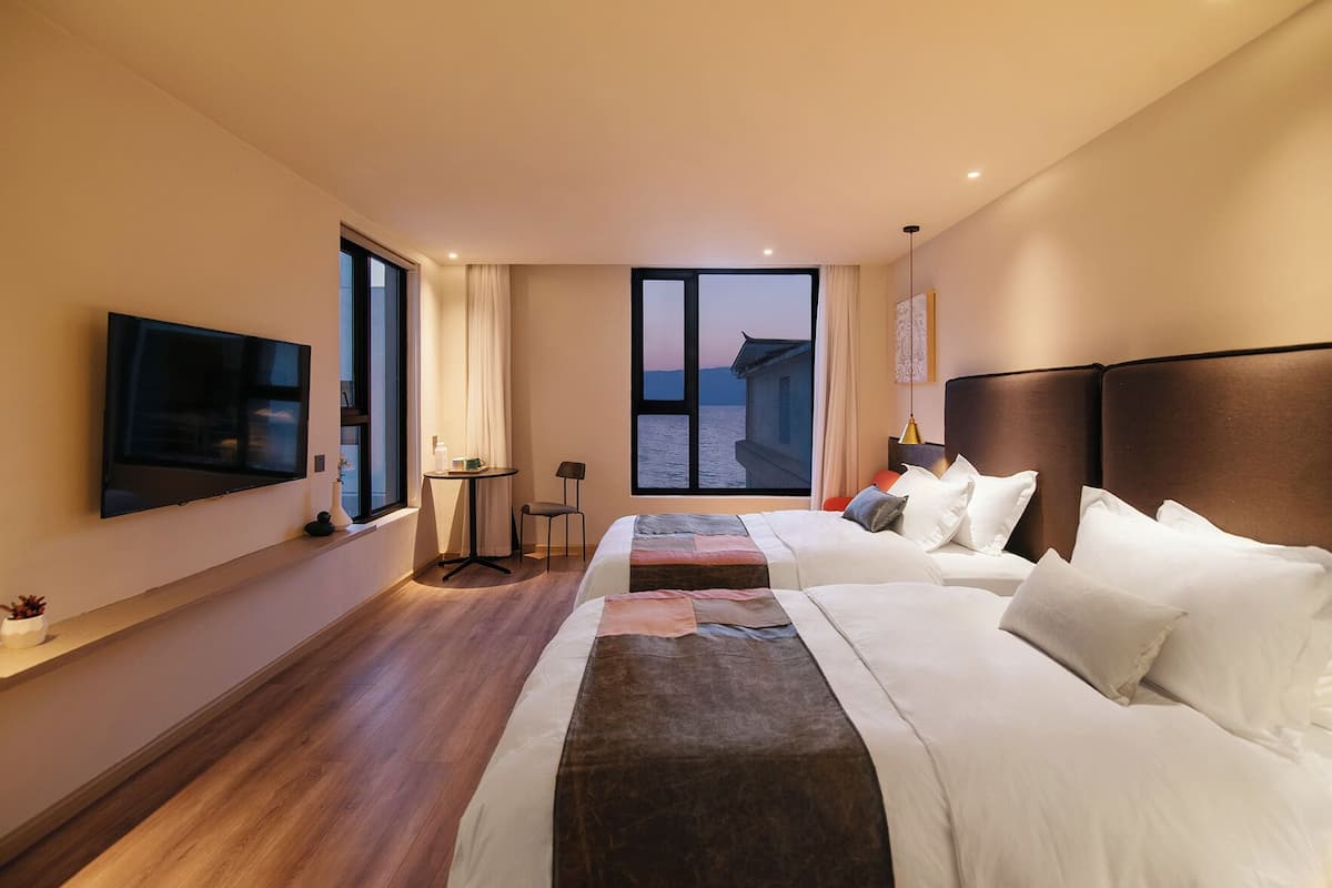 Een hotelkamer met twee bedden, een televisie, een tafeltje, een stoel en uitzicht op zee.