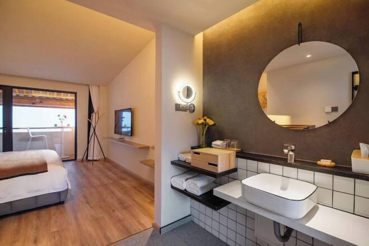Een moderne hotelkamer met een bed, een badkamer met een grote spiegel, een wastafel en een balkon met uitzicht.