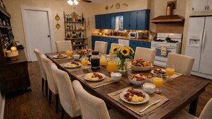Een eetkamer met een houten tafel gedekt voor het ontbijt, inclusief borden met eten, glazen sinaasappelsap en een vaas met zonnebloemen.