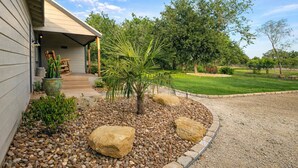 Een huis met een overdekte veranda, een kleine palmboom en een grindpad.