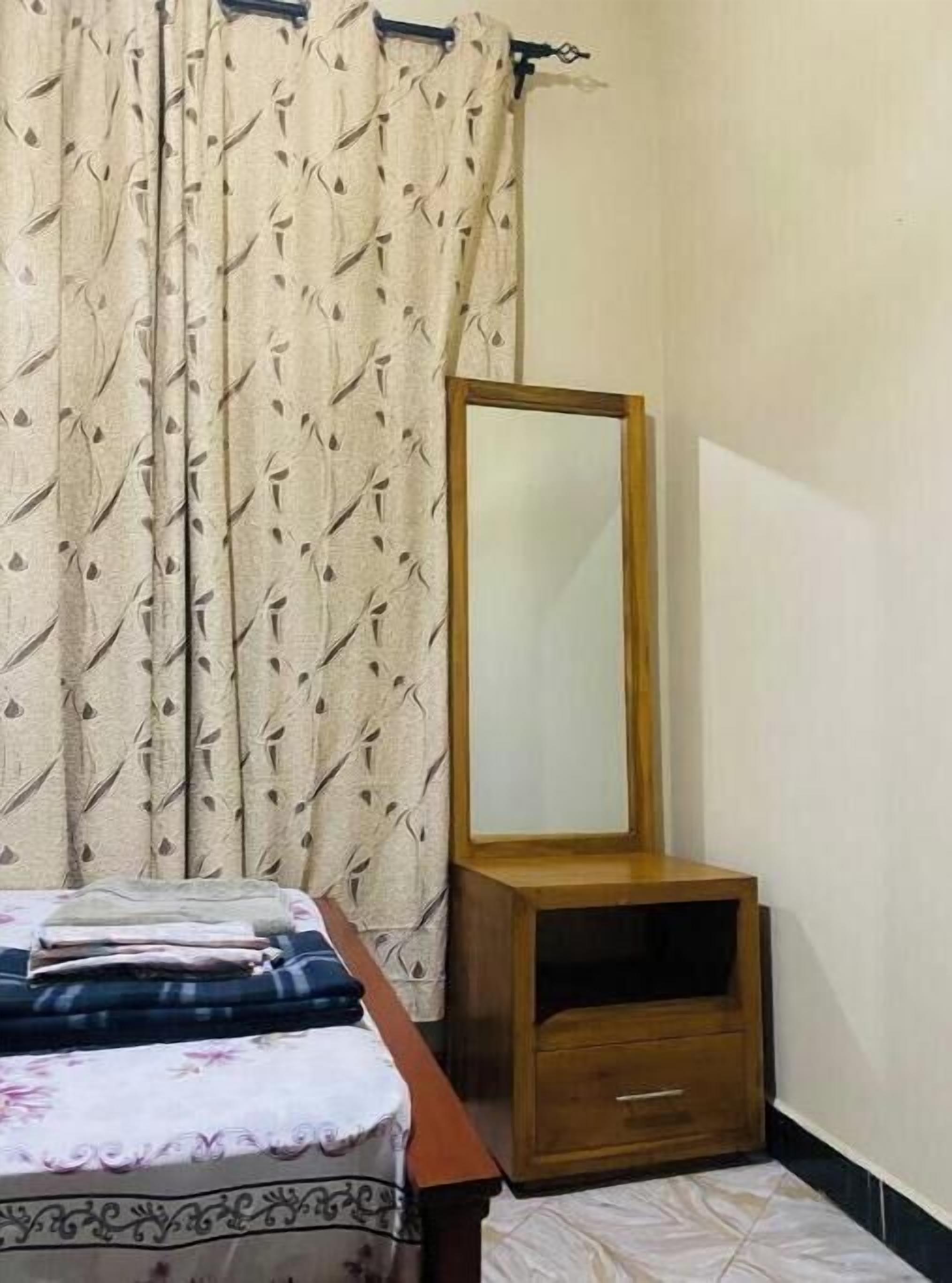 Une chambre à coucher avec un lit, une commode en bois, un miroir et des rideaux à motifs.
