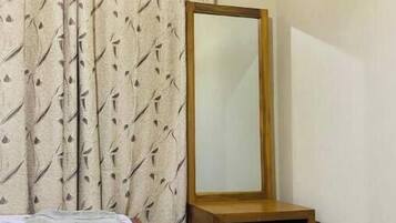 Une chambre à coucher avec un lit, une commode en bois, un miroir et des rideaux à motifs.