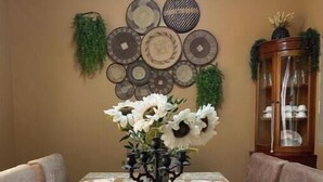 A dining table with a floral centerpiece, surrounded by chairs, and a wall decorated with circular plates and greenery. - 4Bedroom Family Home in Moshi (Moshi)