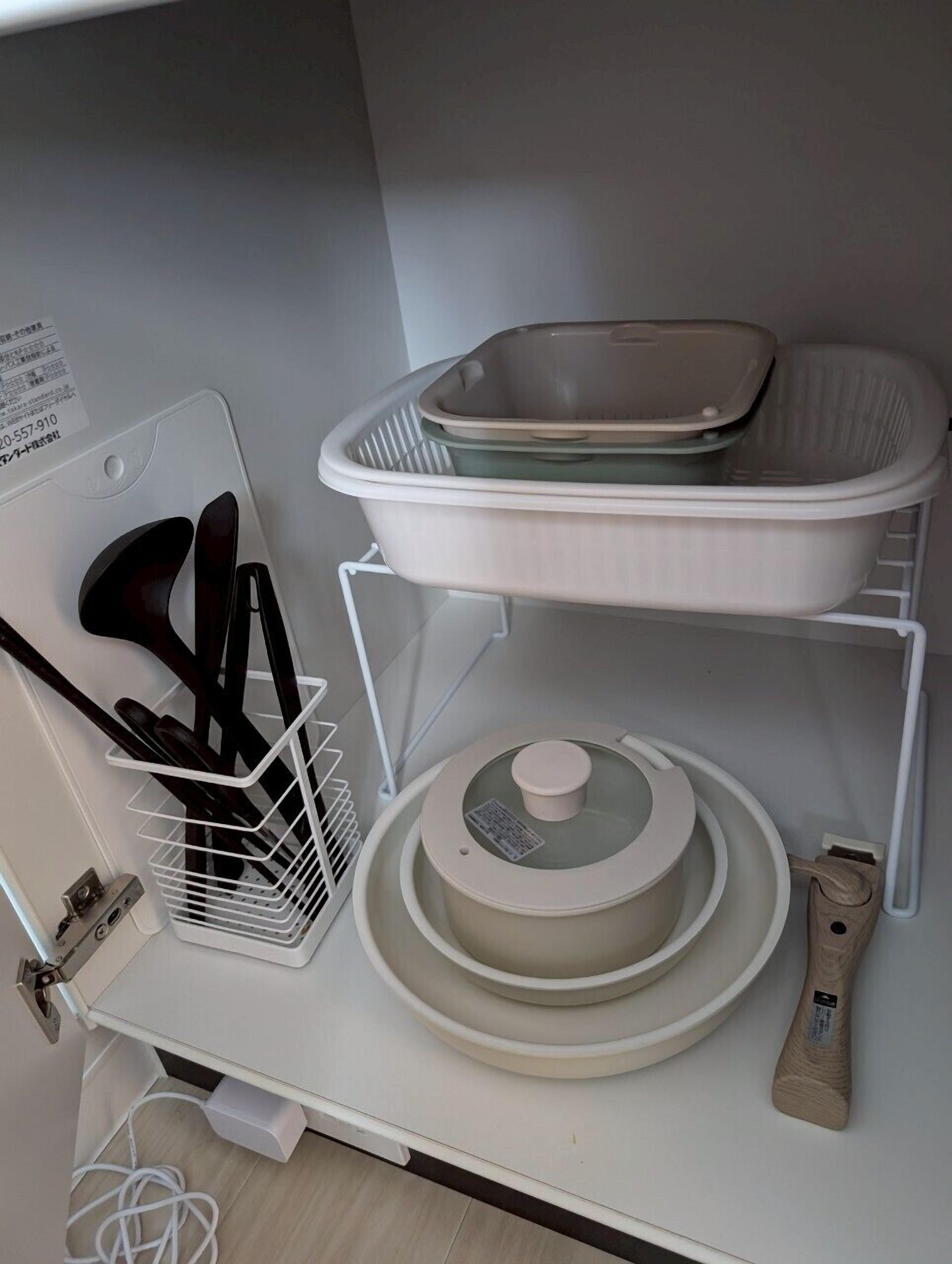 A kitchen counter with a white sink, a dish rack with utensils, a white tray, and a pot with a lid.
