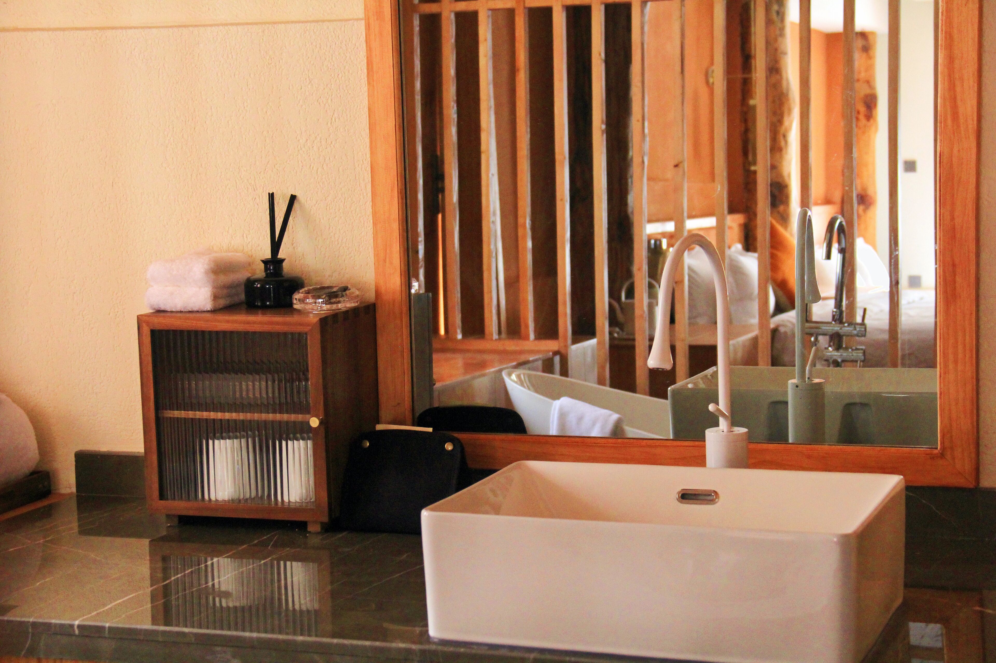 A bathroom with a large mirror, a white sink, and a wooden shelf with toiletries.