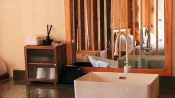A bathroom with a large mirror, a white sink, and a wooden shelf with toiletries.