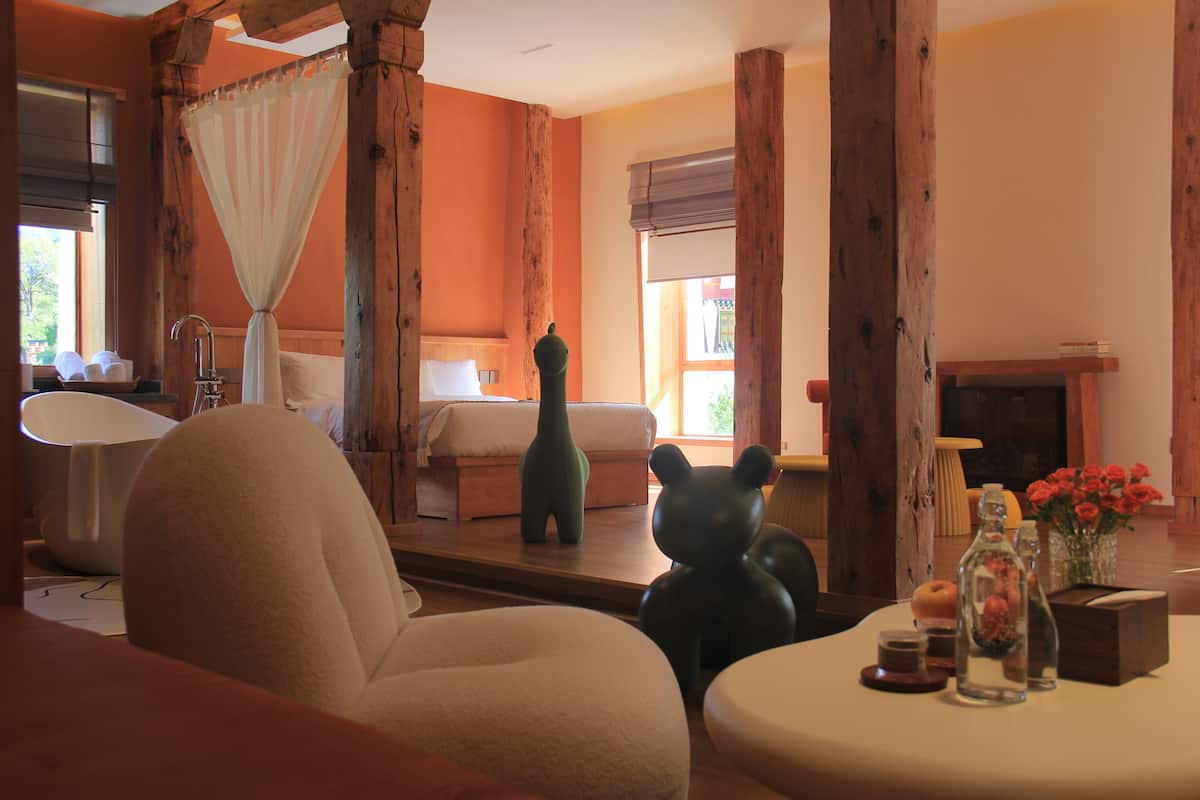 Una habitación acogedora con una cama, un ventanal grande, una chimenea y una mesa con adornos.
