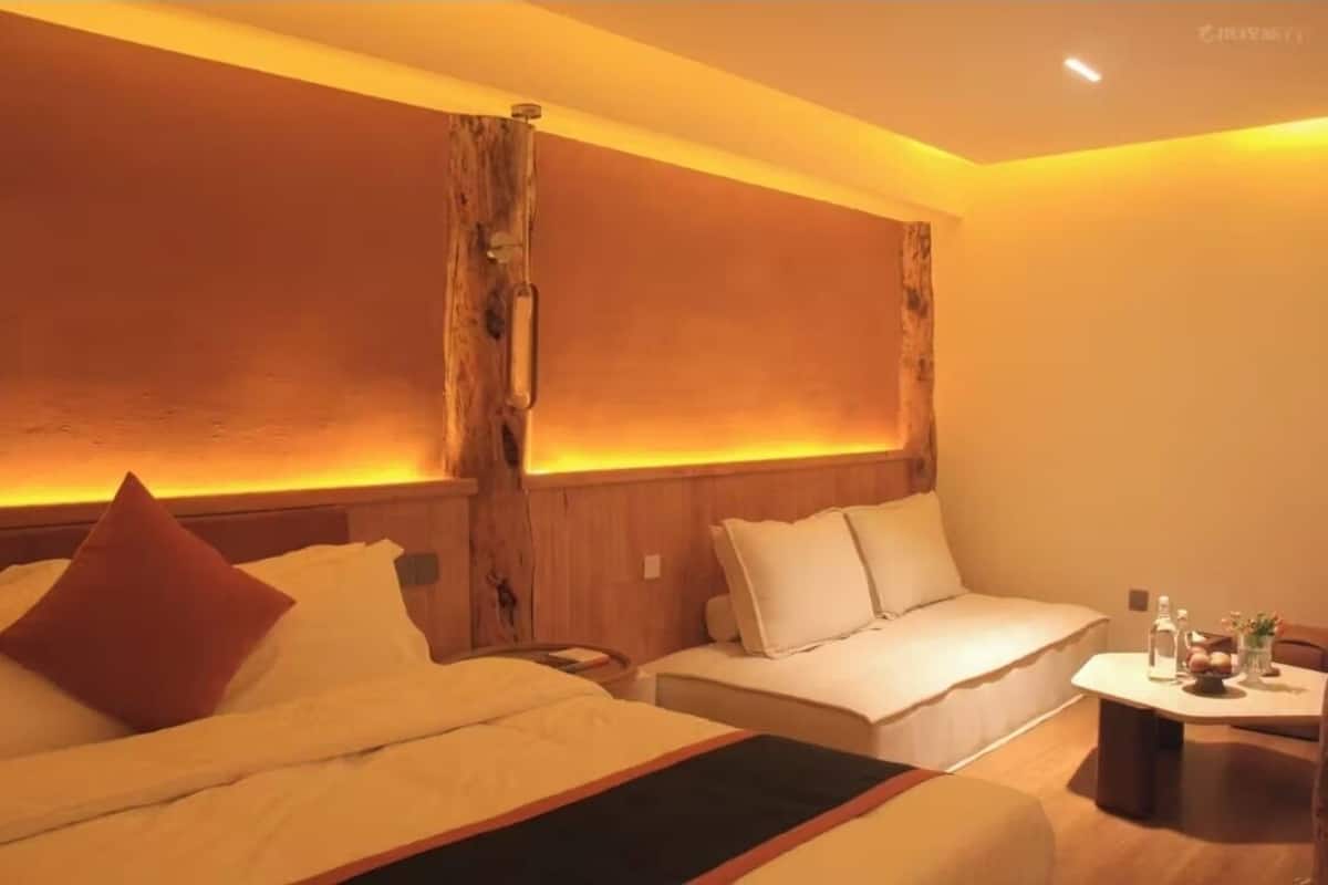 Habitación de hotel con dos camas, una mesita con un florero y botellas, y una pared decorativa de madera.