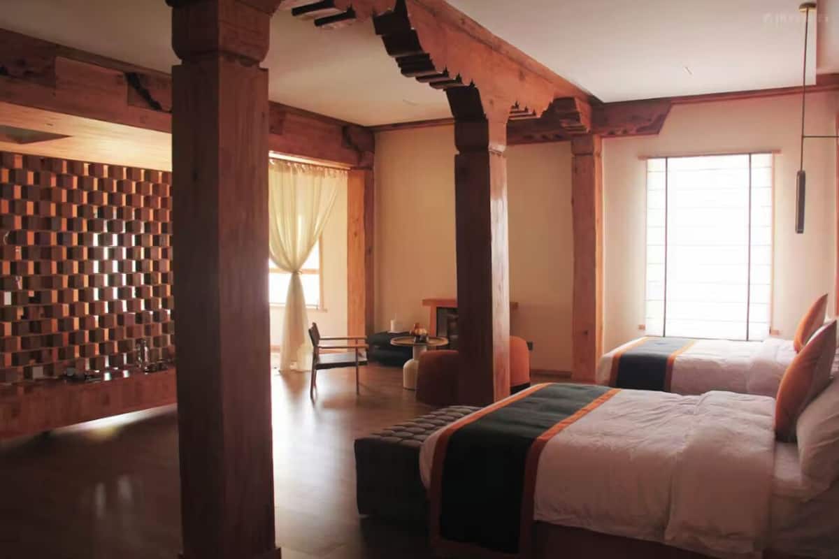 Habitación de hotel con dos camas, una pared de madera, un ventanal grande y una mesita pequeña.