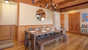 A dining area with a wooden table set for six, a bench, and a chandelier. - Ski In Ski Out Big Sky Chalet (Big Sky)