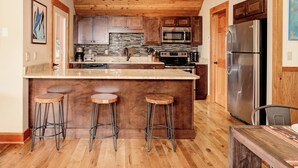 A kitchen with wooden cabinets, a stainless steel refrigerator, a microwave, a stove, and a large island with stools. - Ski In Ski Out Big Sky Chalet (Big Sky)
