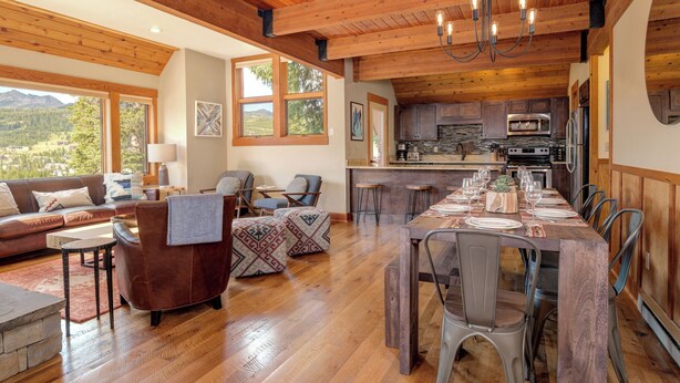 A spacious living area with a wooden ceiling, a dining table set for six, and a kitchen with modern appliances. - Ski In Ski Out Big Sky Chalet (Big Sky)