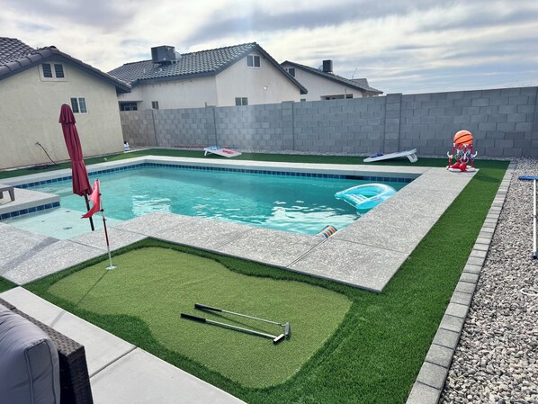 Una piscina con un deck circundante, un pequeño espacio con césped y un aro de baloncesto.
