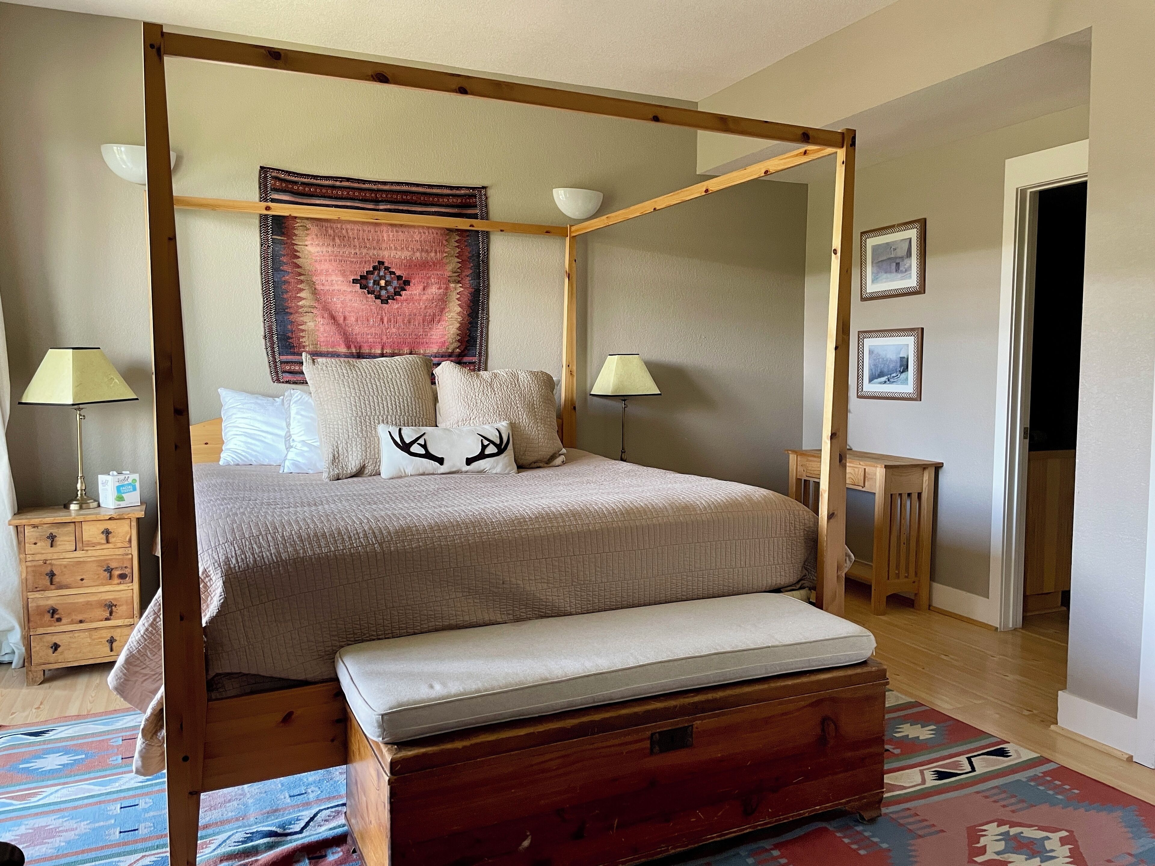 A four-poster bed with a bench, bedside tables, a wall tapestry, and framed pictures.