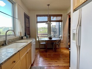 A kitchen with wooden cabinets, a granite countertop, a sink, a dining table with chairs, and a refrigerator. - Moonlight Basin | Ski in & Out | Lone Peak Views (Big Sky)