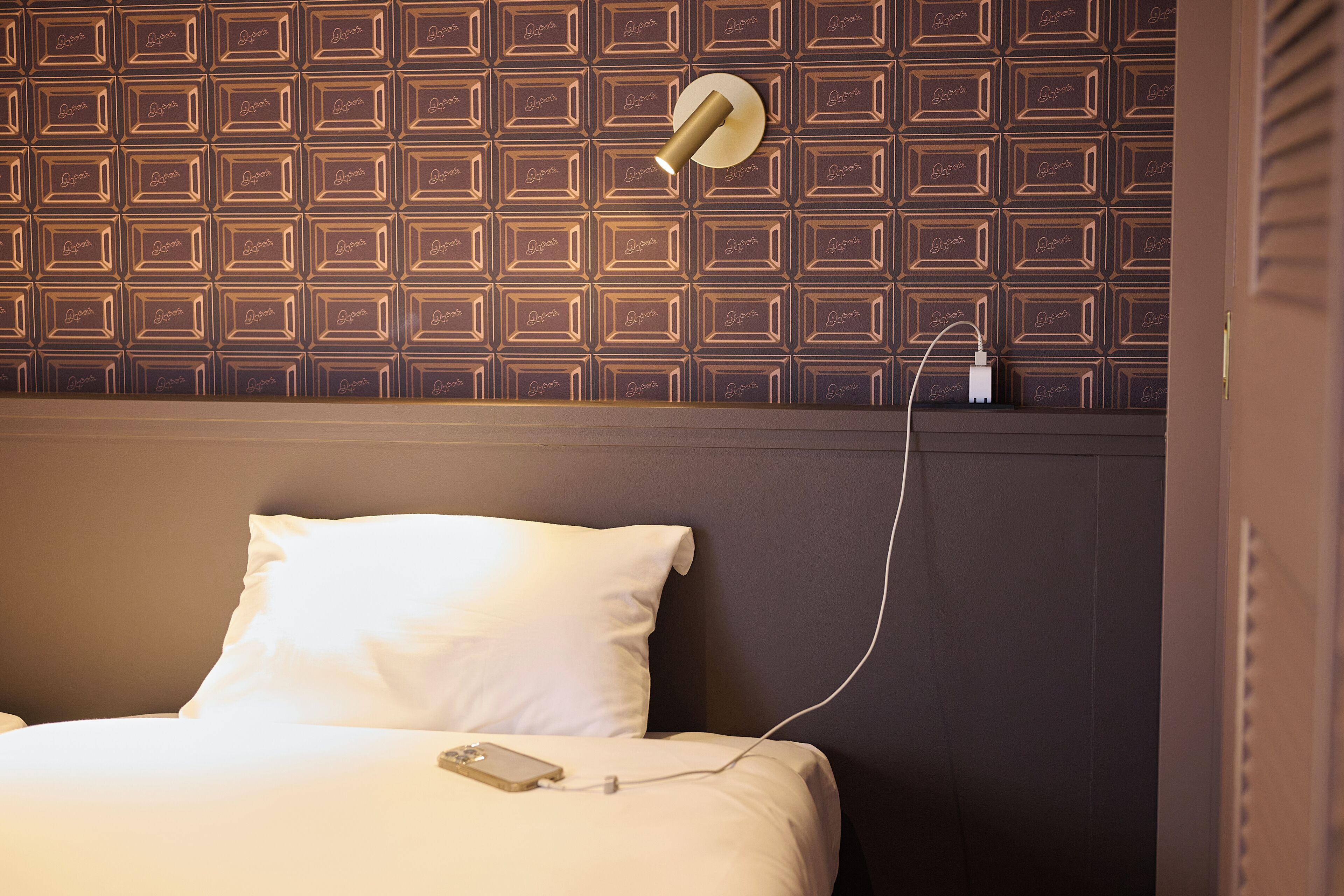 A hotel room with a patterned wall, a bed with white bedding, and a wall-mounted light fixture.