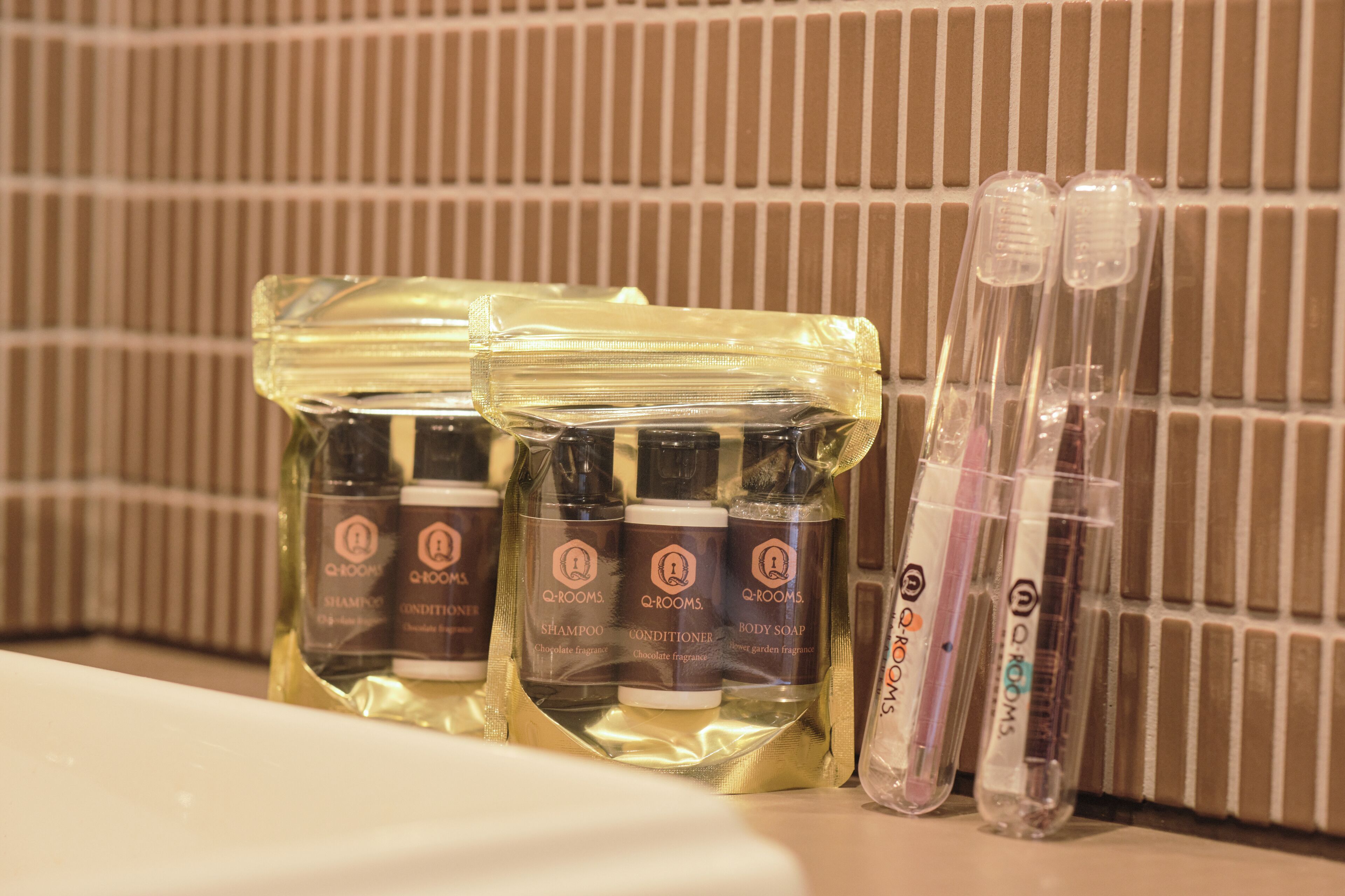 A bathroom with toiletries including shampoo, conditioner, and body soap in clear plastic bags, and two toothbrushes in clear plastic cases.