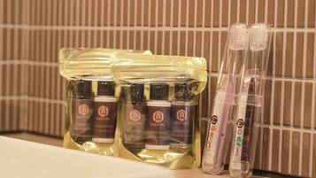A bathroom with toiletries including shampoo, conditioner, and body soap in clear plastic bags, and two toothbrushes in clear plastic cases.