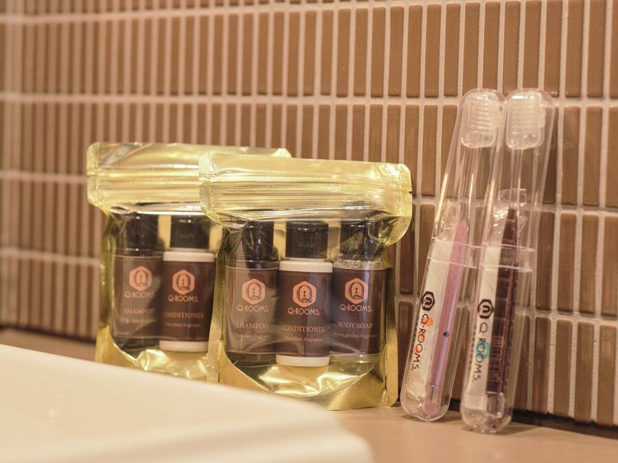 A bathroom with toiletries including shampoo, conditioner, and body soap in clear plastic bags, and two toothbrushes in clear plastic cases.