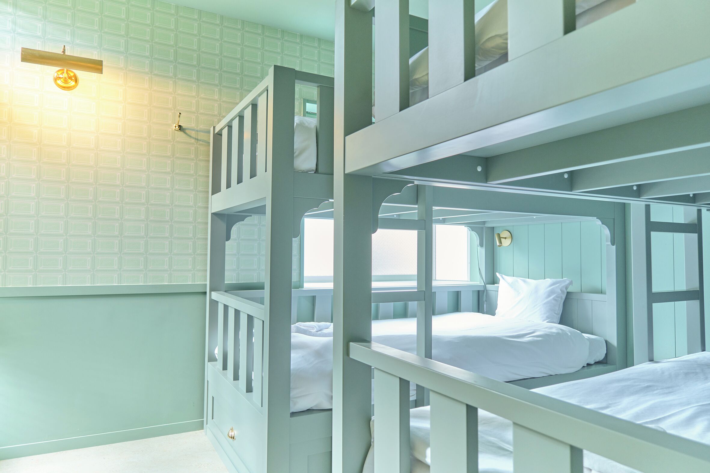 A bunk bed room with a light green wall and a small window.
