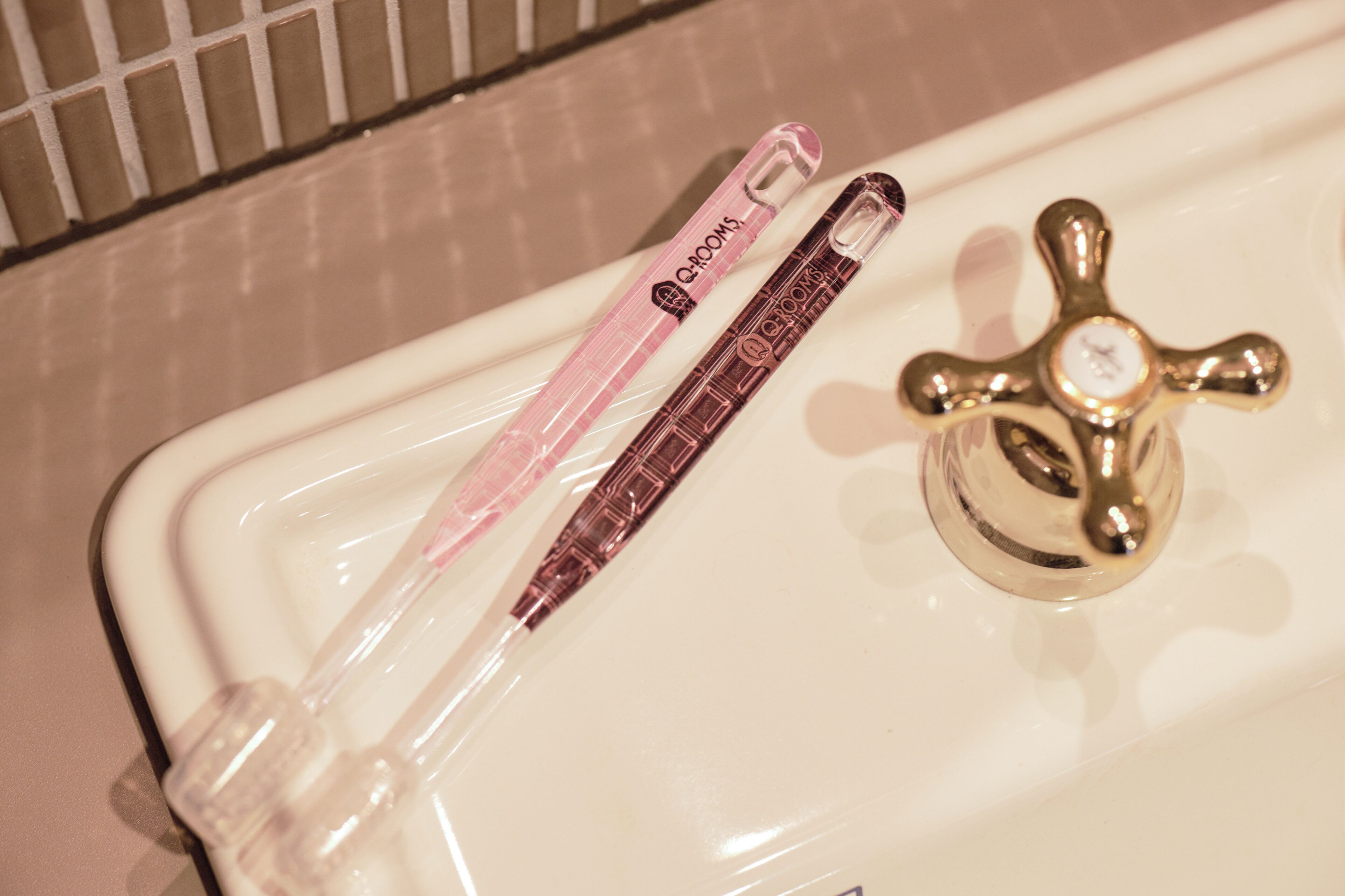 A bathroom sink with a gold faucet and a pink bottle of hand soap.
