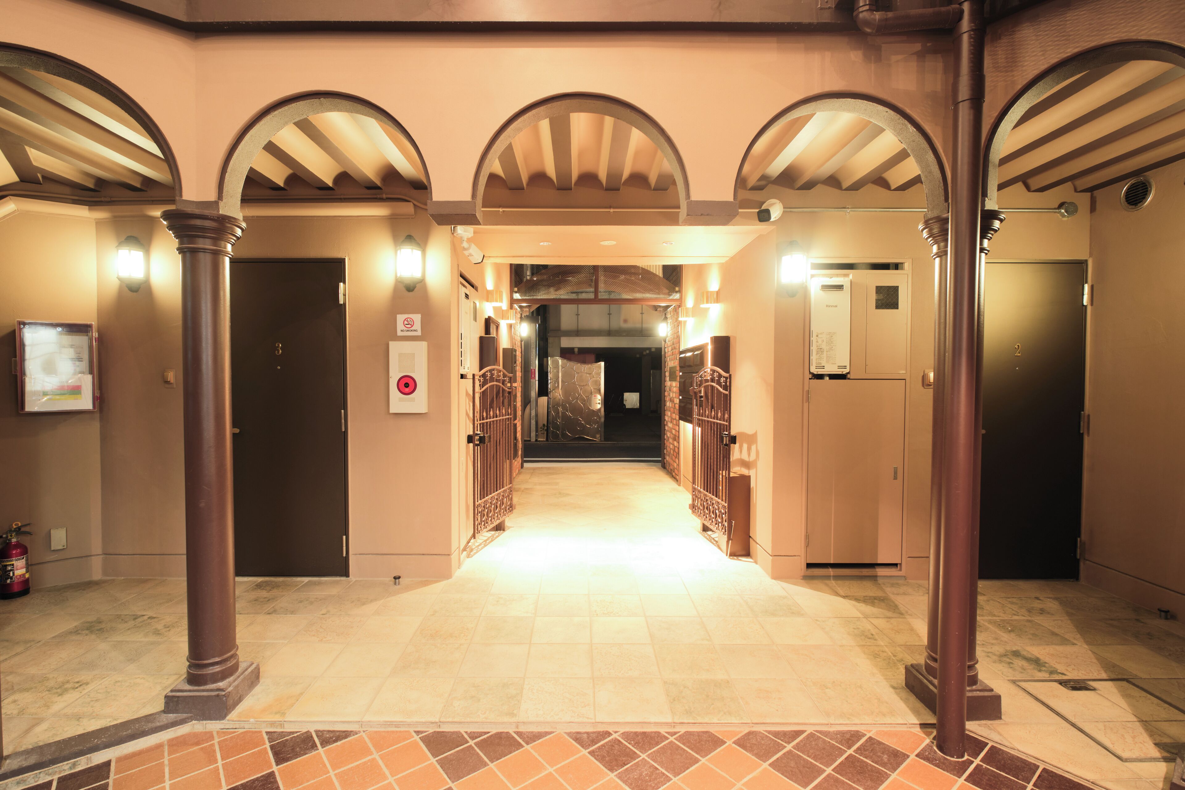 A hotel corridor with arched ceilings, a tiled floor, and a fire extinguisher on the left.