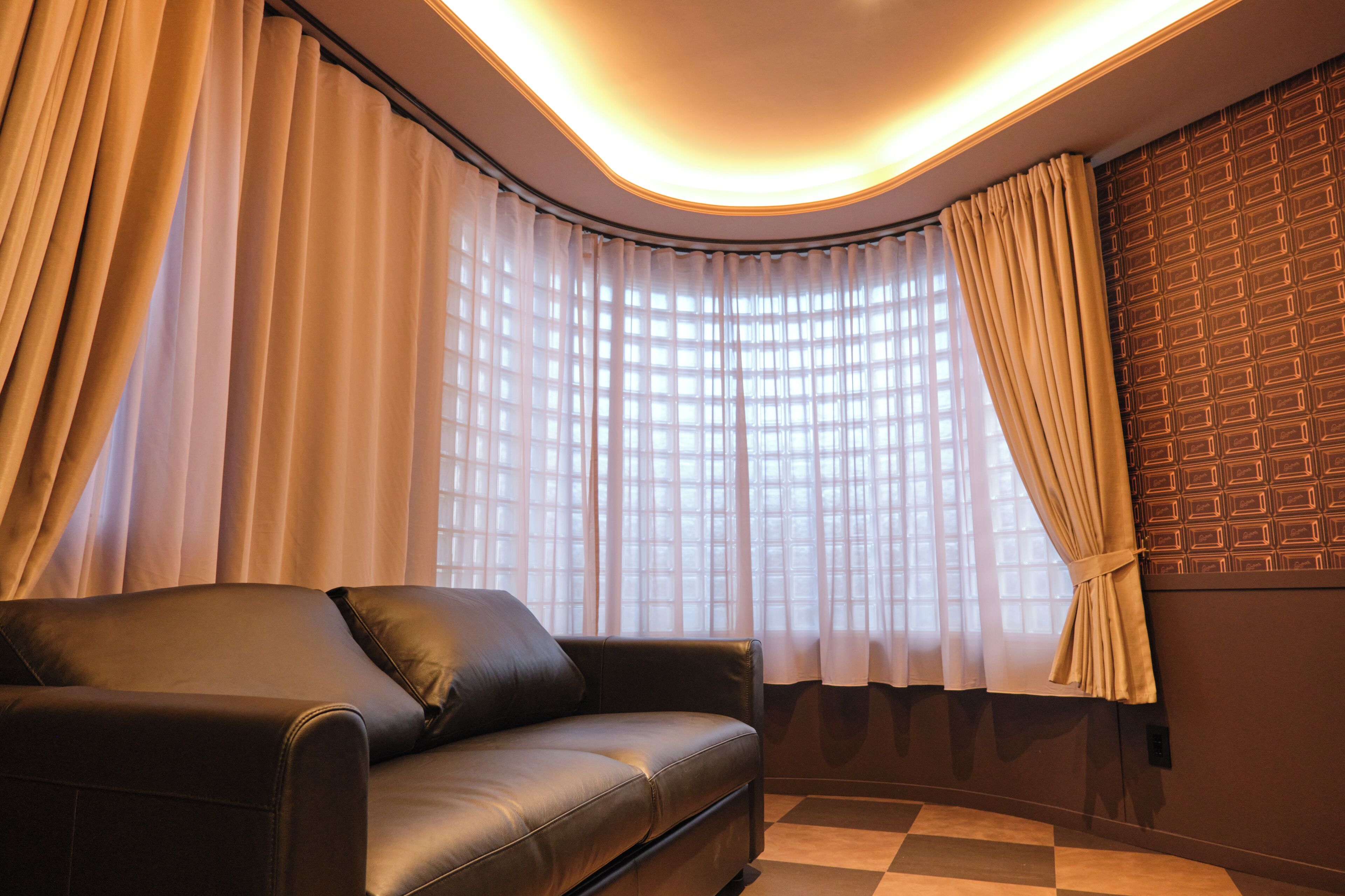 A modern room with a leather sofa, large windows with sheer curtains, and a patterned wall.